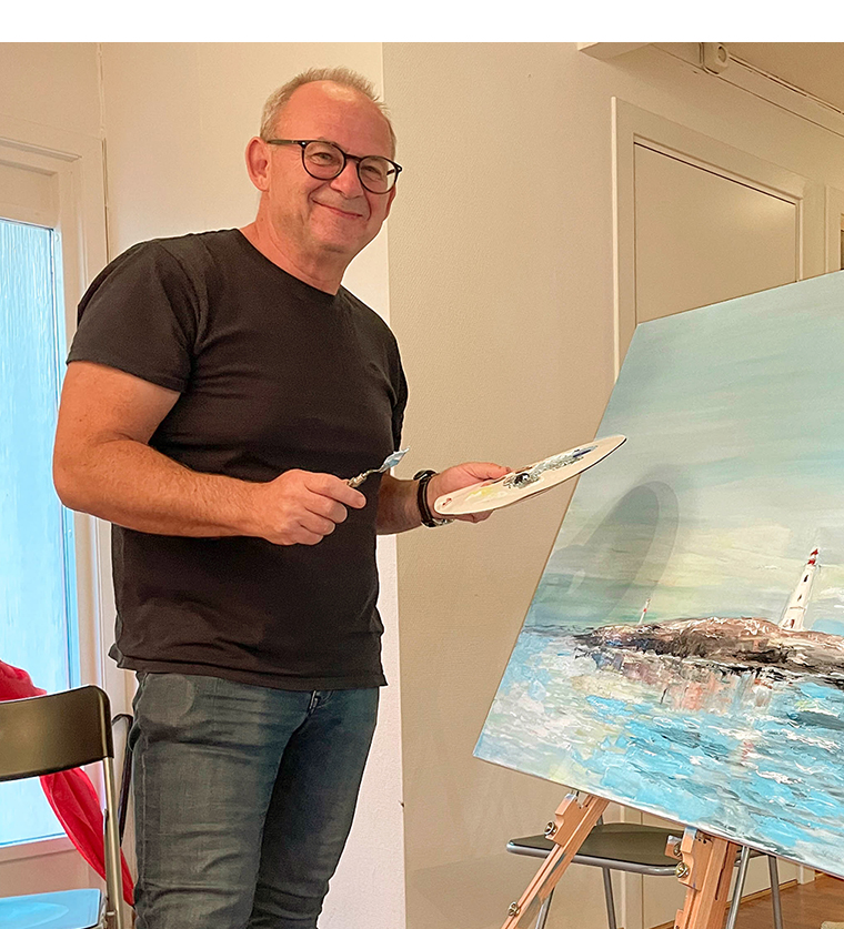 Kunstneren Arnfinn Øynes smiler mot kameraet foran et lerret.